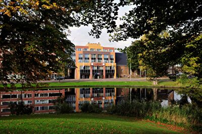 Amrâth Hotel Alkmaar with colorful facades and reflection in a water feature, surrounded by greenery.